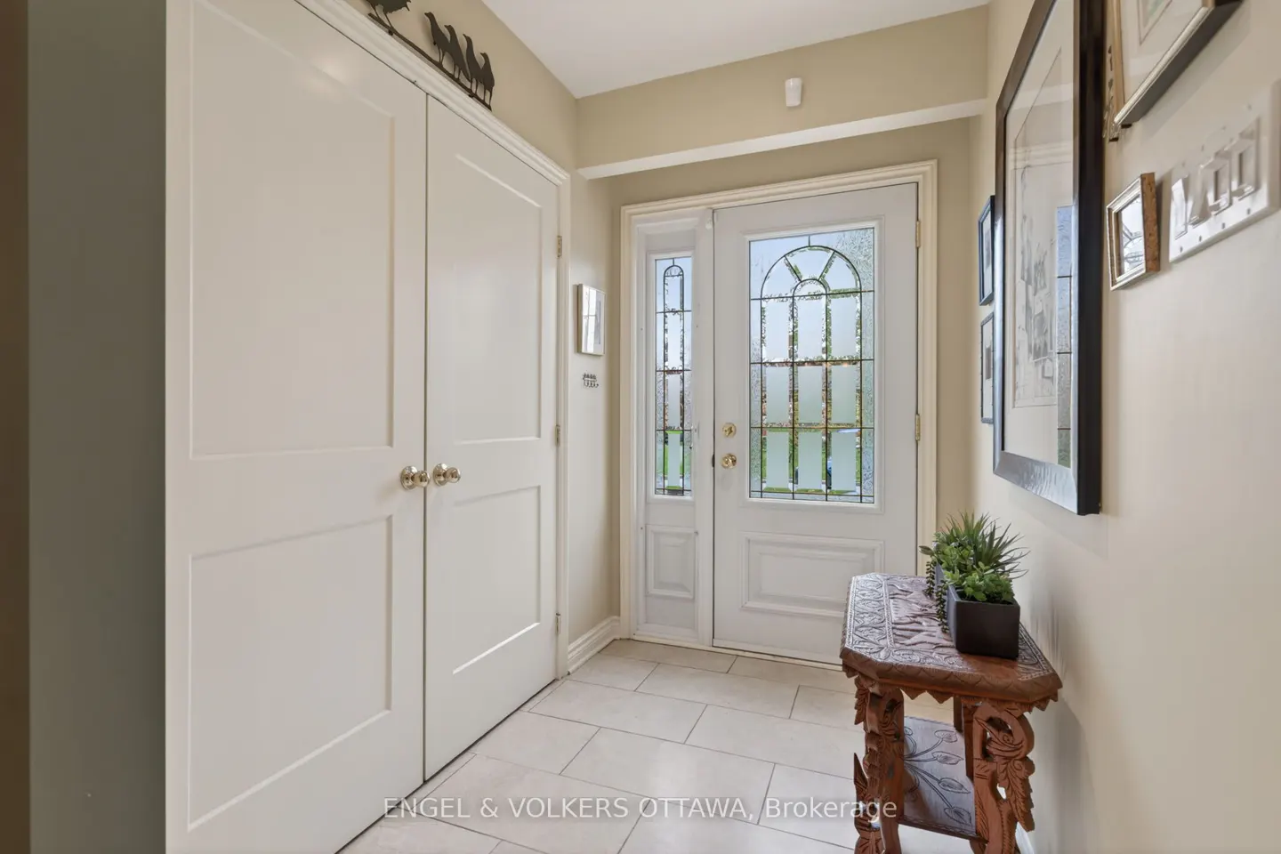 Foyer with white closet doors, a white front door with glass, and a carved wooden table with a plant.
