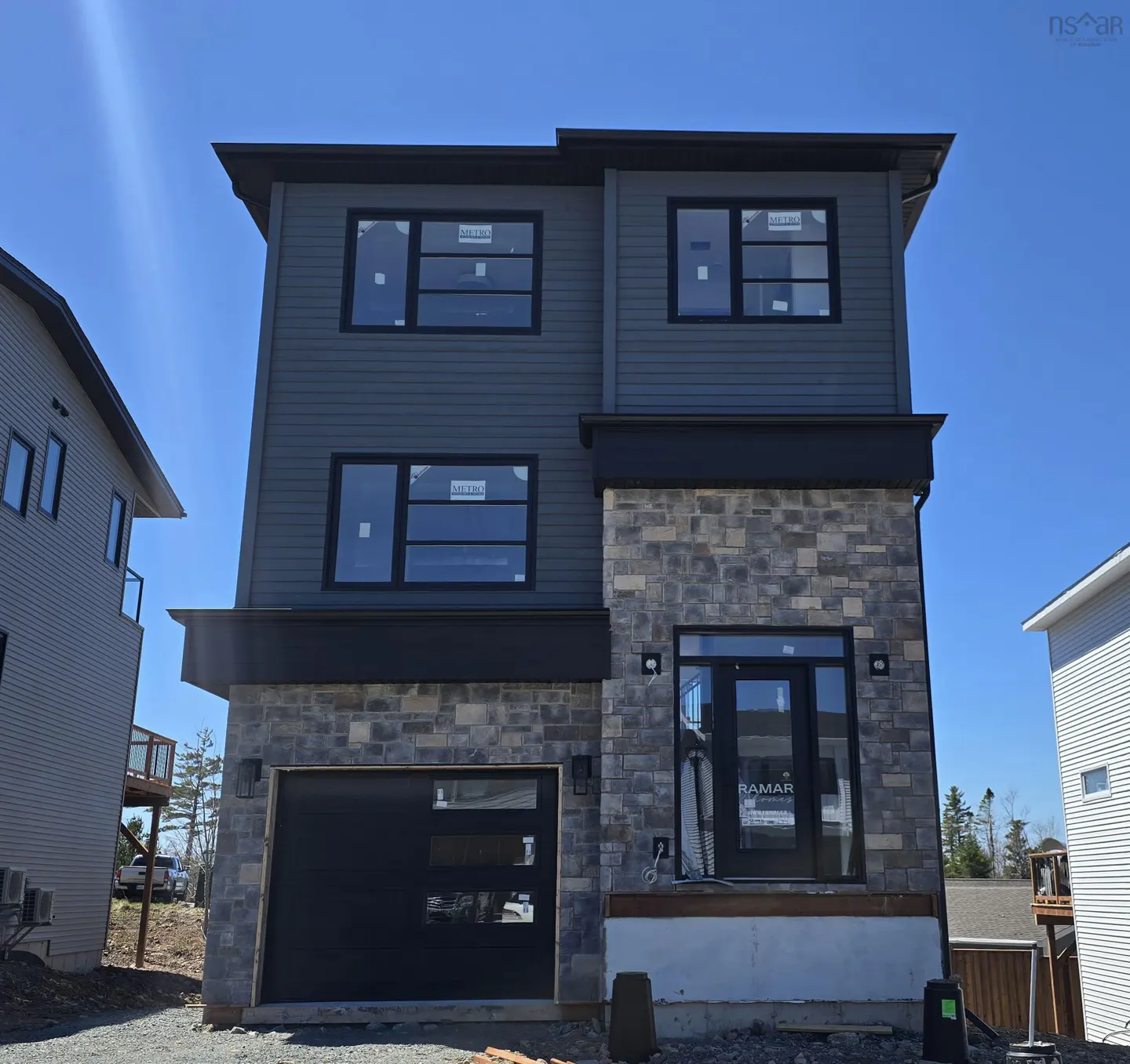 Two-story house with gray siding and stone facade. Black trim accents windows and garage door. Blue sky background.