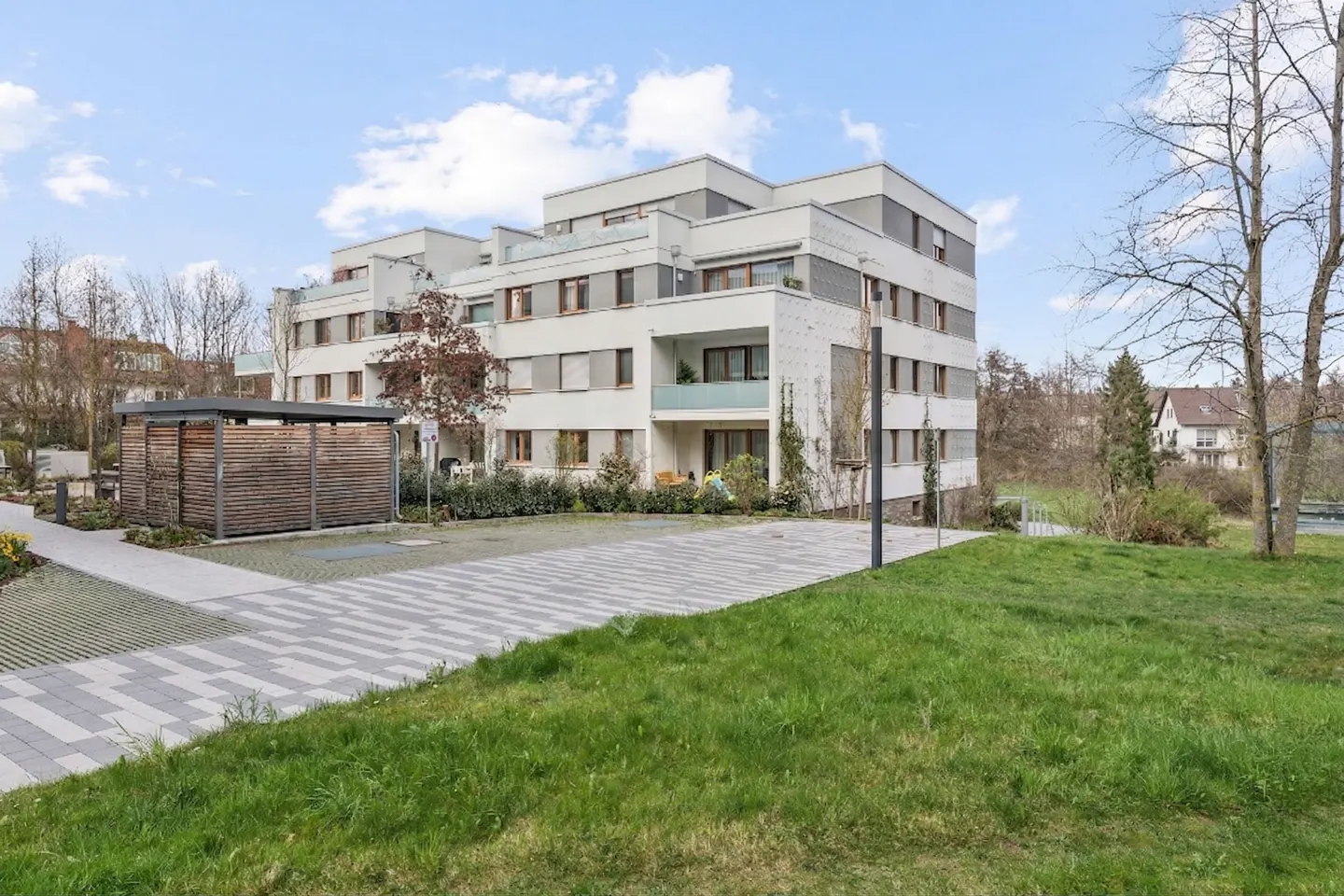 Modern white apartment building with gray accents, a wooden carport, and a green lawn under a blue sky.