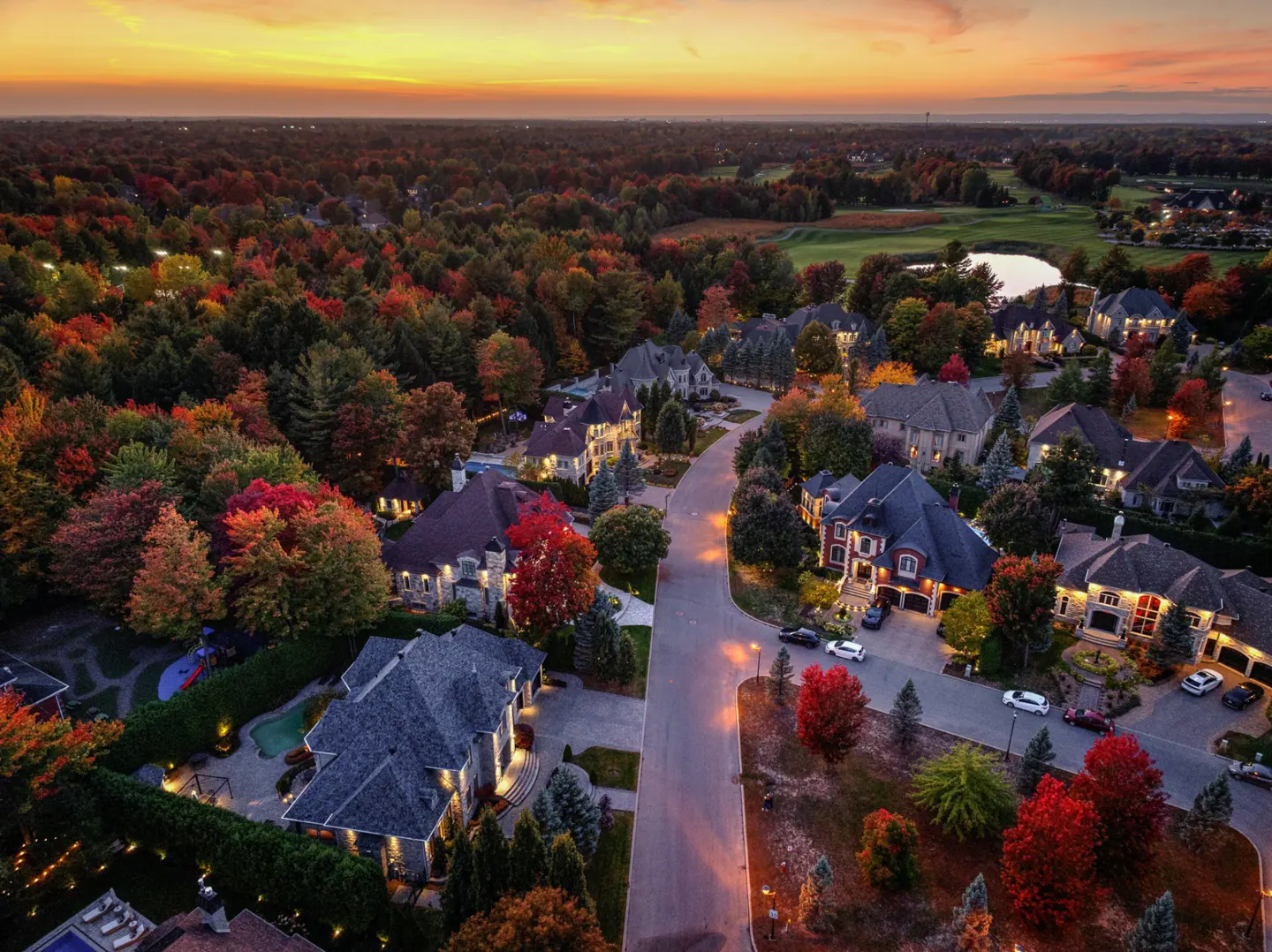Aerial view of a luxury neighborhood in autumn, with colorful trees and large houses at sunset.