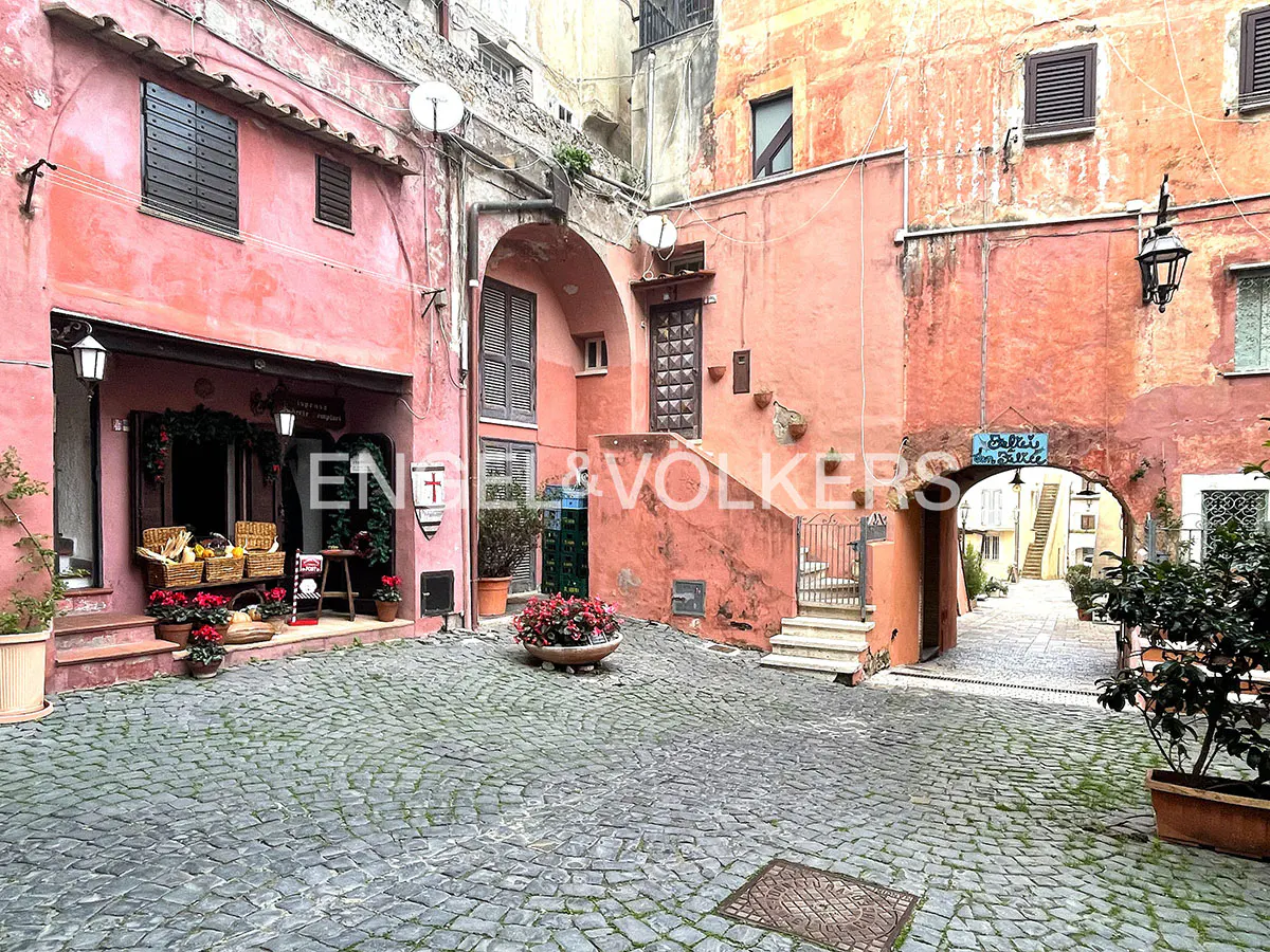 Cobblestone courtyard surrounded by rustic pink and orange buildings with arched entryways and potted flowers.