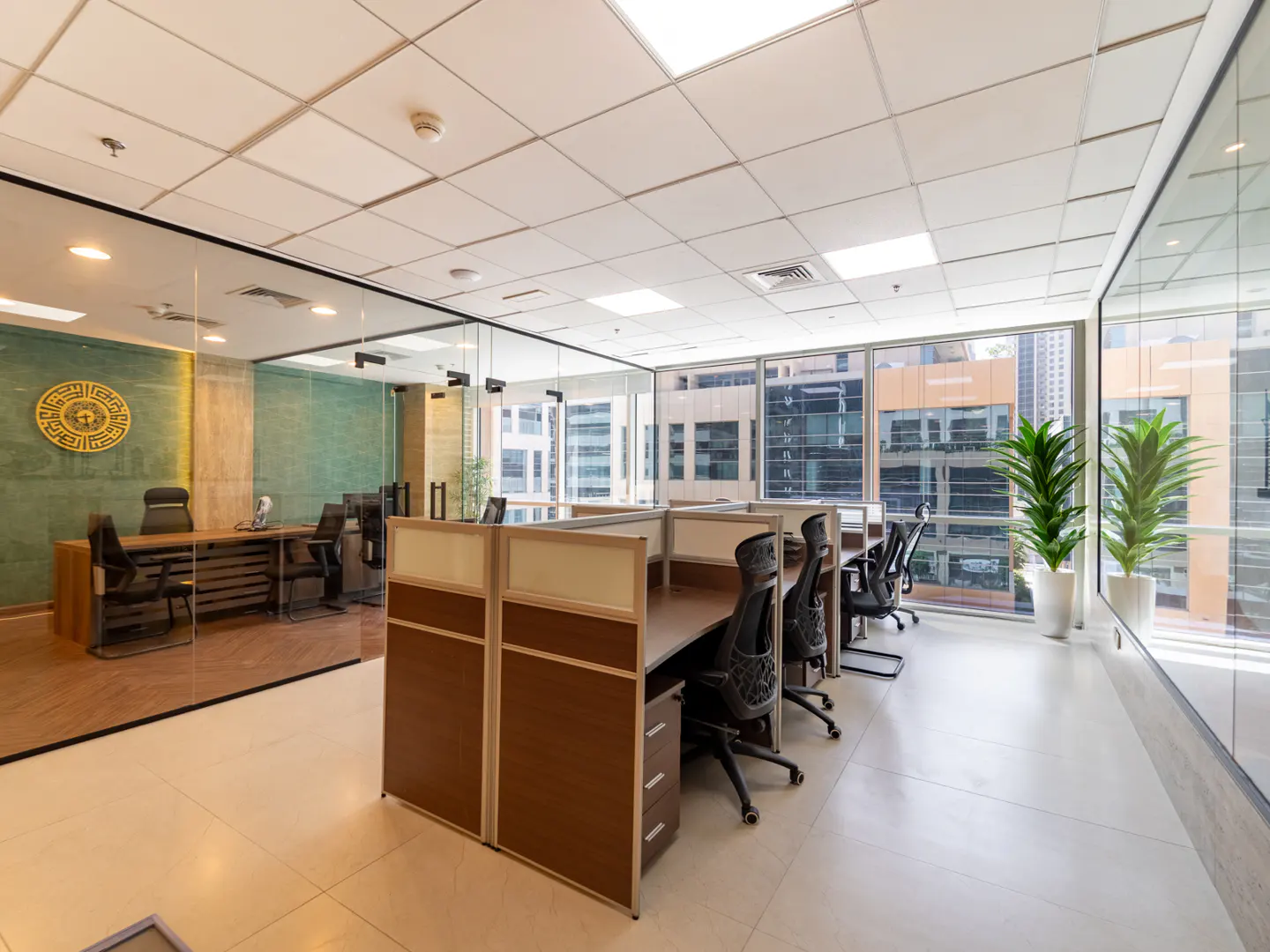 Office space with desks, chairs, and cubicles. A glass-walled office is visible in the background. Large windows offer a city view.