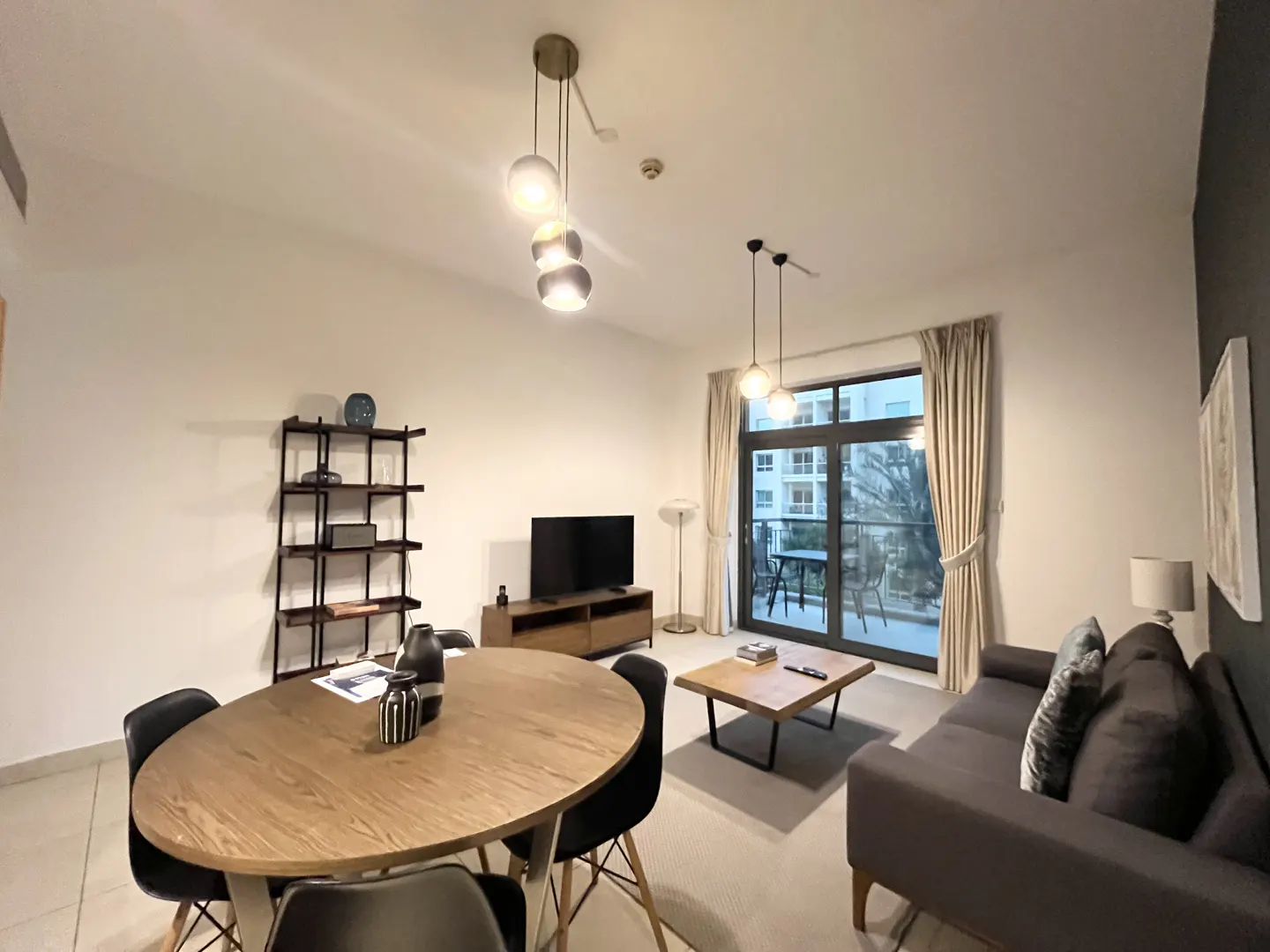 A modern living room with a wood dining table, black chairs, gray sofa, and balcony access.