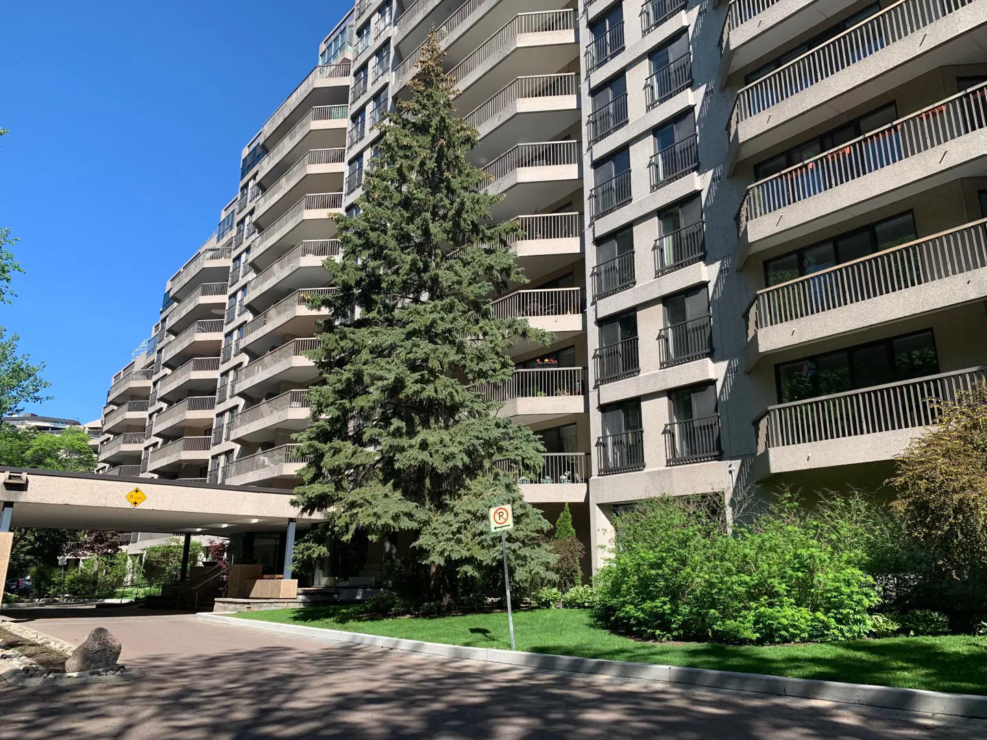 Exterior view of a beige condo building with balconies, a covered entrance, and green trees.