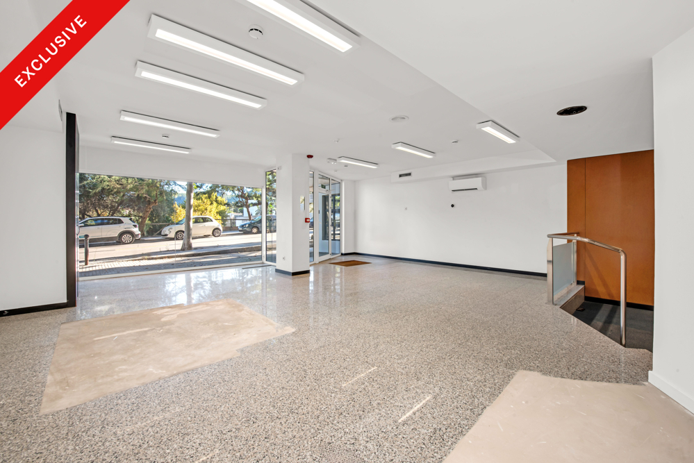 Bright, empty commercial space with white walls, speckled stone flooring, recessed lighting, and a large street-view window. [AI-generated text]