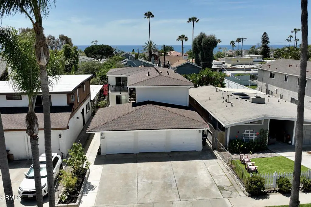 Aerial view of a white two-story house with a brown roof, a three-car garage, and a concrete driveway near the ocean.