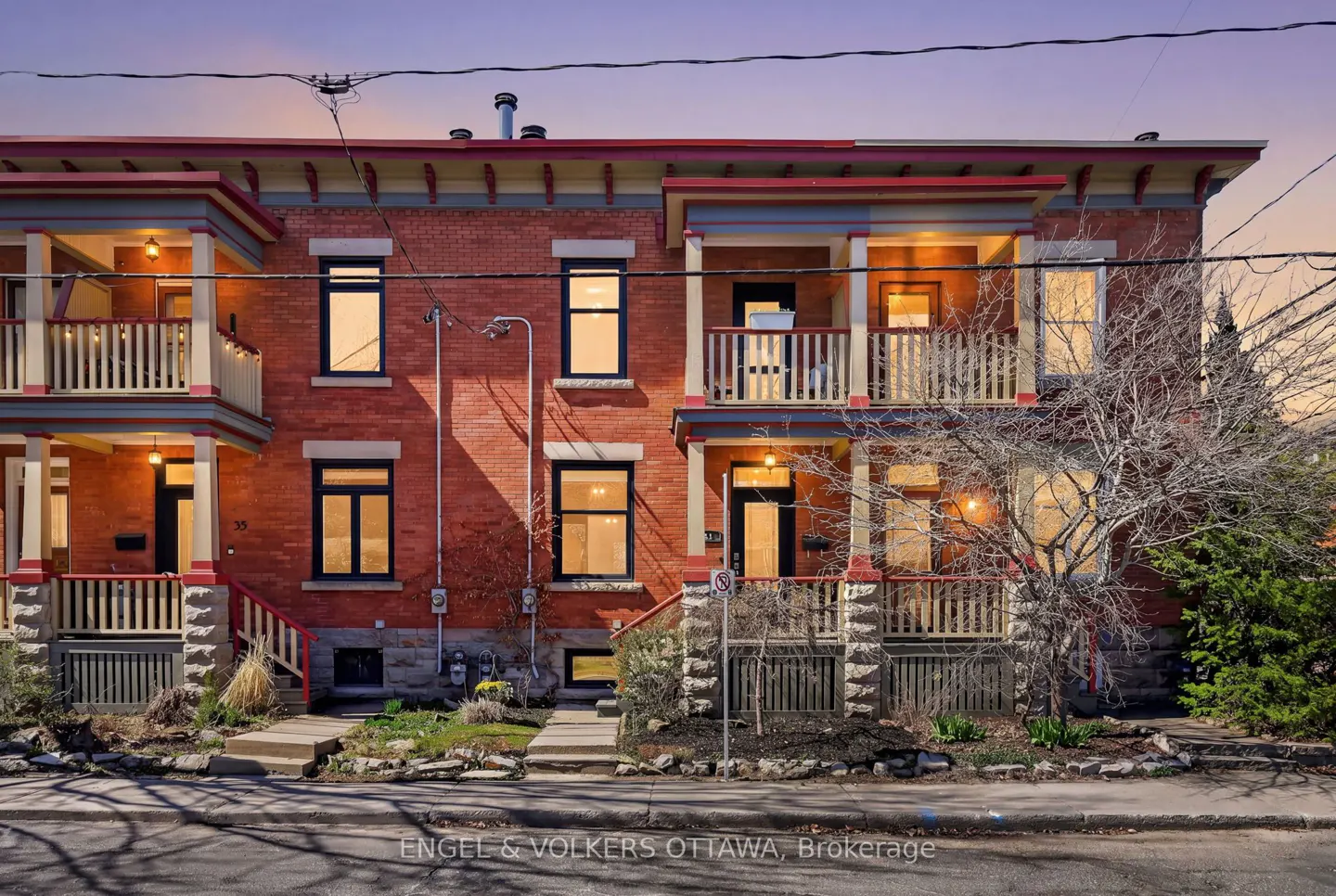 Exterior view of two-story red brick townhouses with balconies and black-framed windows under a twilight sky.