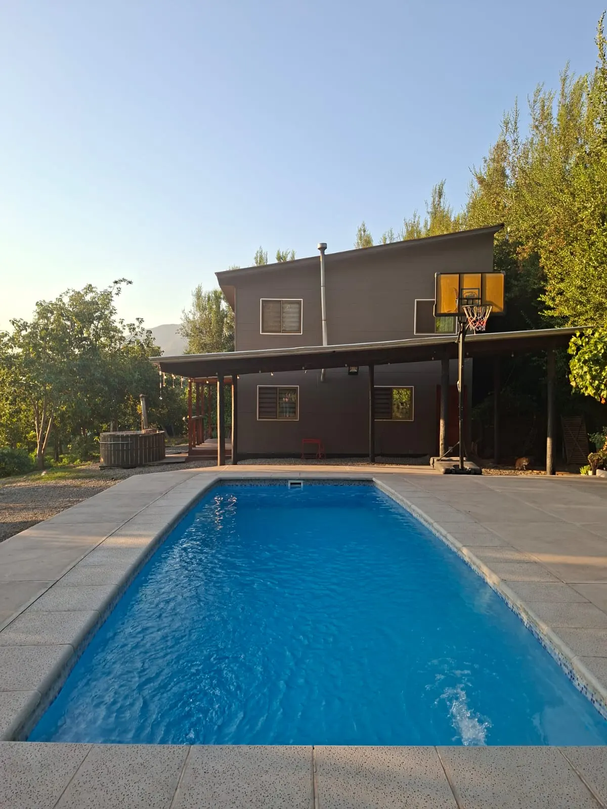 A modern gray house with a blue swimming pool and a basketball hoop in the backyard.