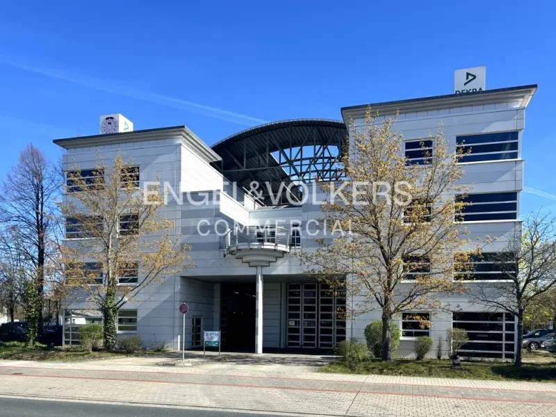 Exterior view of a modern, light gray commercial building with dark windows and Engel & Volkers signage.