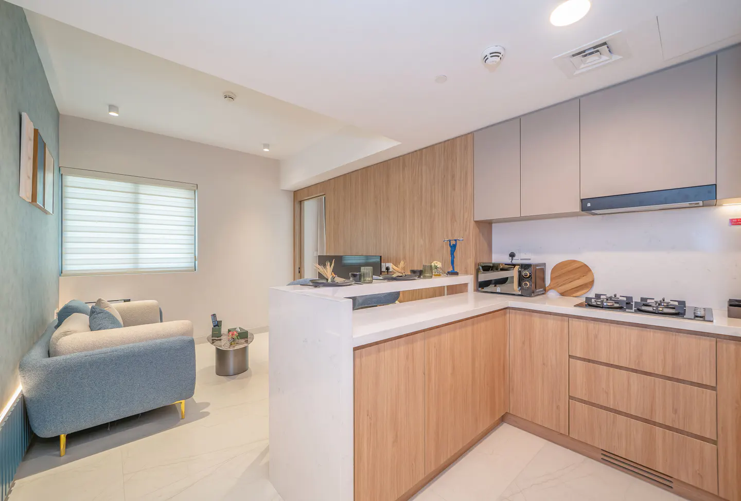 A modern apartment interior with a blue sofa, white marble floors, and a kitchen with wood cabinets.