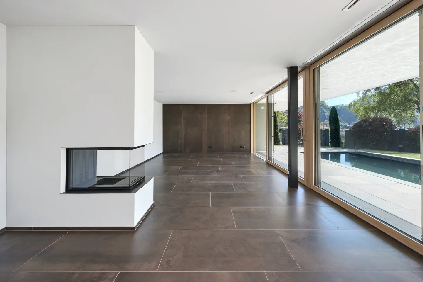 A modern living room with brown tile floors, a white fireplace, and large windows overlooking a pool.