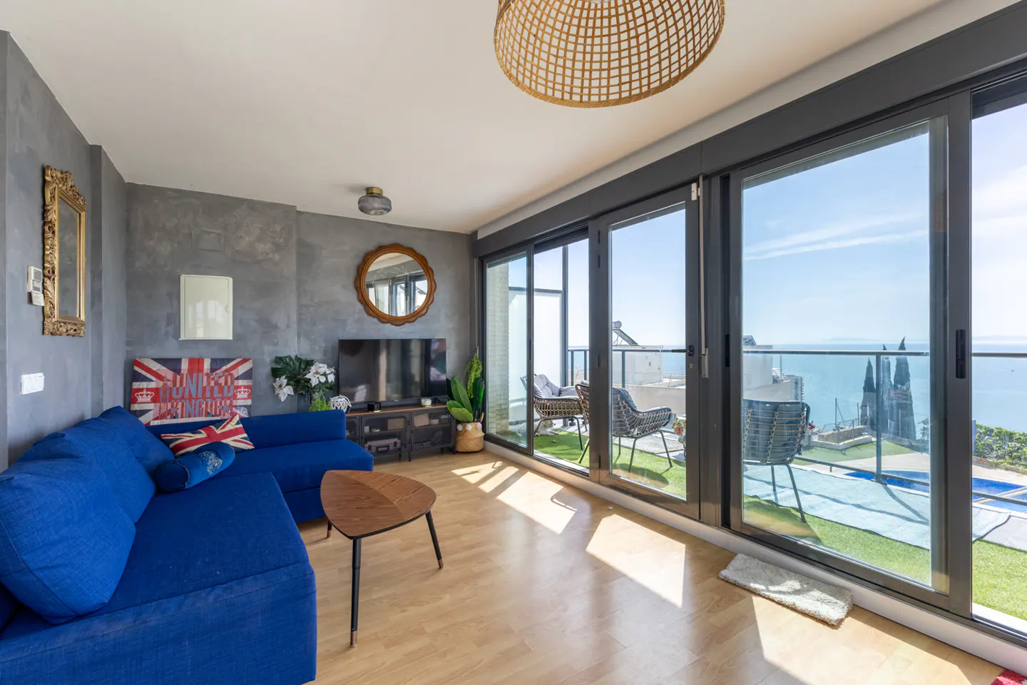 Living room with blue sofa, wood floors, and sliding glass doors to a balcony with ocean views.
