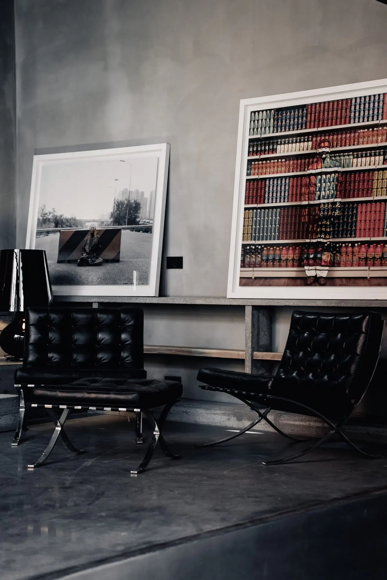 Interior view of a gray room with two black leather Barcelona chairs and framed art on a shelf.