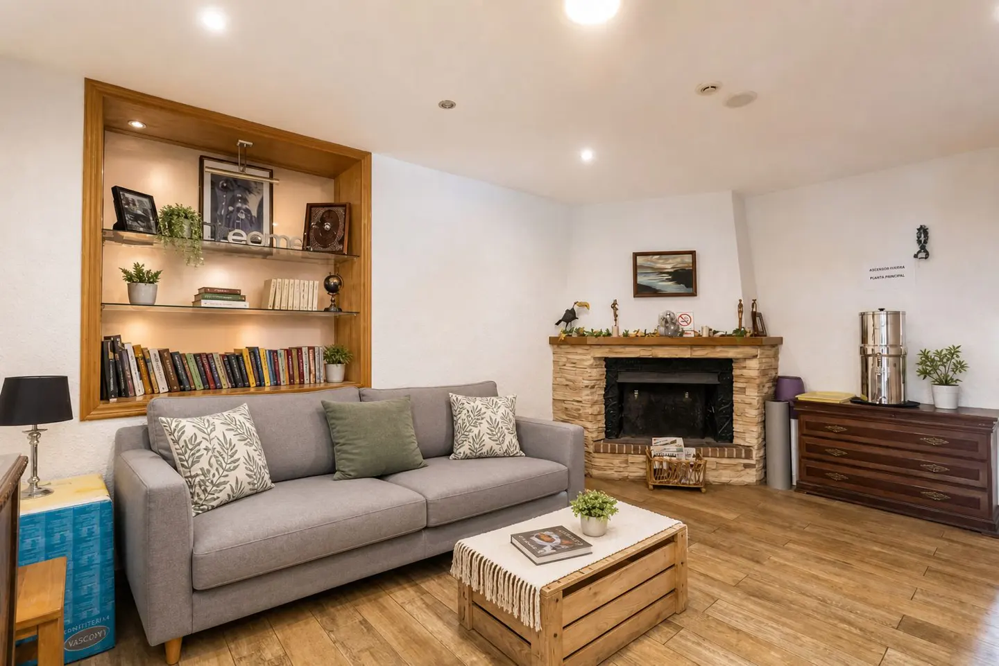 Living room with a gray sofa, wooden bookshelf, and stone fireplace. A wooden crate serves as a coffee table.