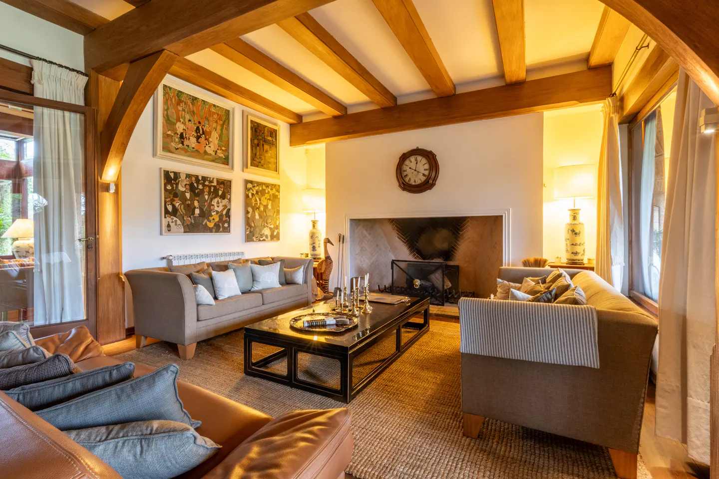 Living room with exposed wood beams, fireplace, sofas, and a black coffee table. Artwork hangs above the sofa.