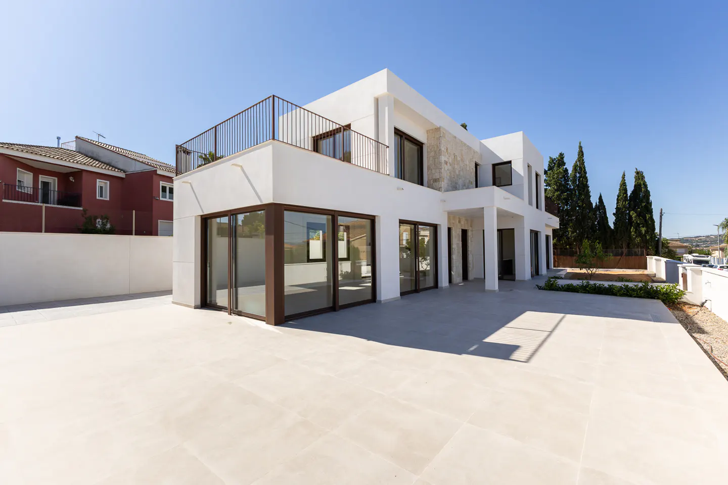 Modern two-story white house with brown window frames and a balcony under a clear blue sky.