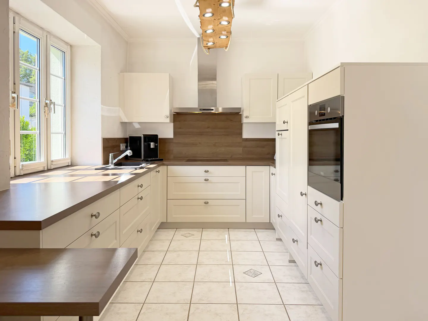Modern kitchen with white cabinets, wood countertops, tiled floor, built-in oven, and a unique wooden ceiling light fixture.