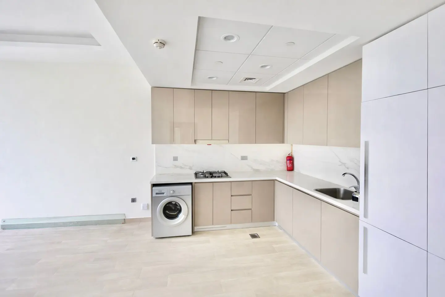 Bright kitchen with beige cabinets, white marble countertops, and a stainless steel sink. A washing machine is next to the gas stove.