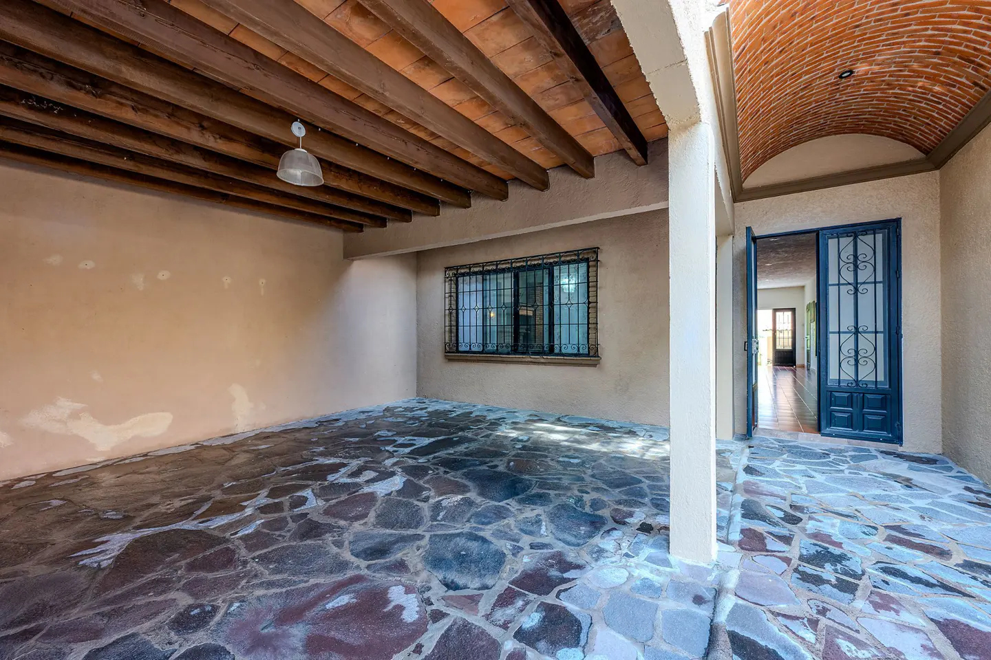Covered patio with stone floor, exposed wood beams, and brick vaulted ceiling. Blue doors lead to the interior.