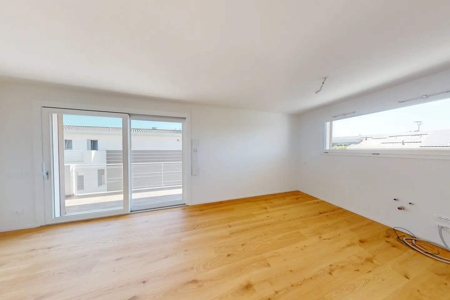 Bright, empty room with light wood floors, white walls, and sliding glass doors to a balcony. A horizontal window is on the right wall.