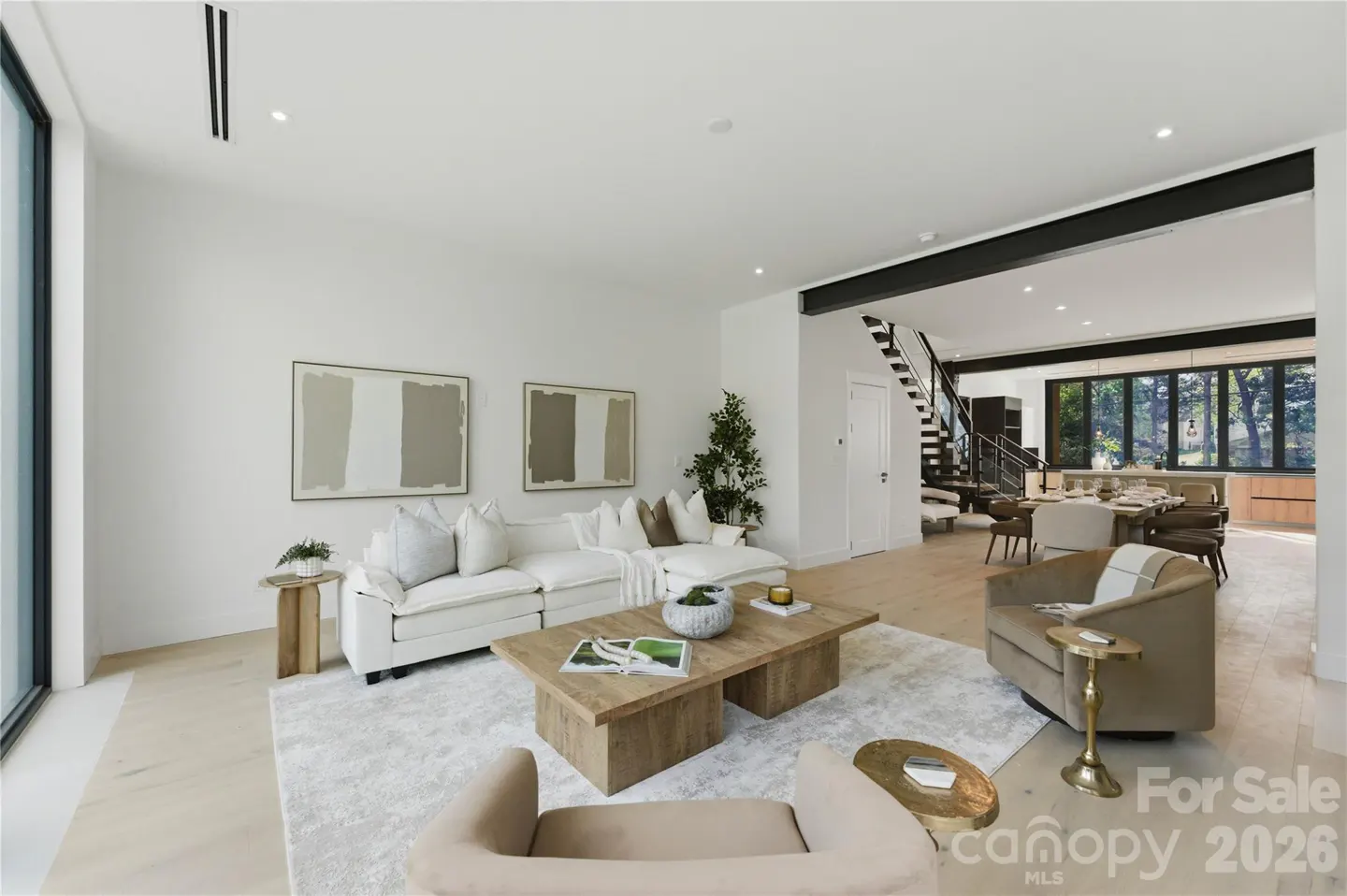 Modern open-concept living room with white sofa, wooden coffee table, beige armchairs, and a view of a dining area.