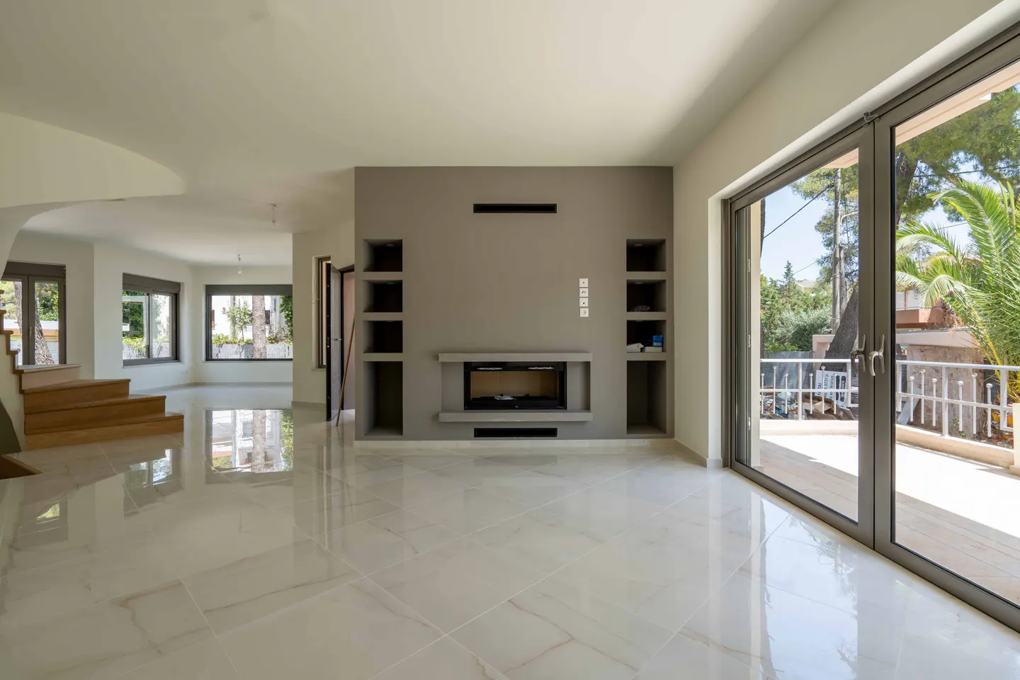 Modern living room with white marble floors, a grey feature wall with a fireplace, and large glass doors to a balcony.