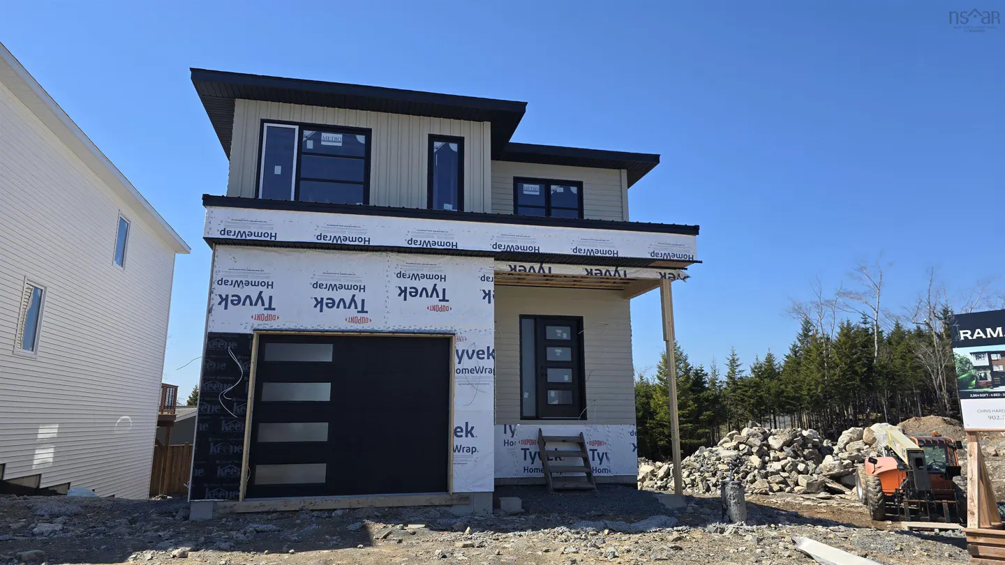 A two-story house under construction with beige siding, black trim, and a black garage door. Tyvek wrap is visible. Blue sky background.