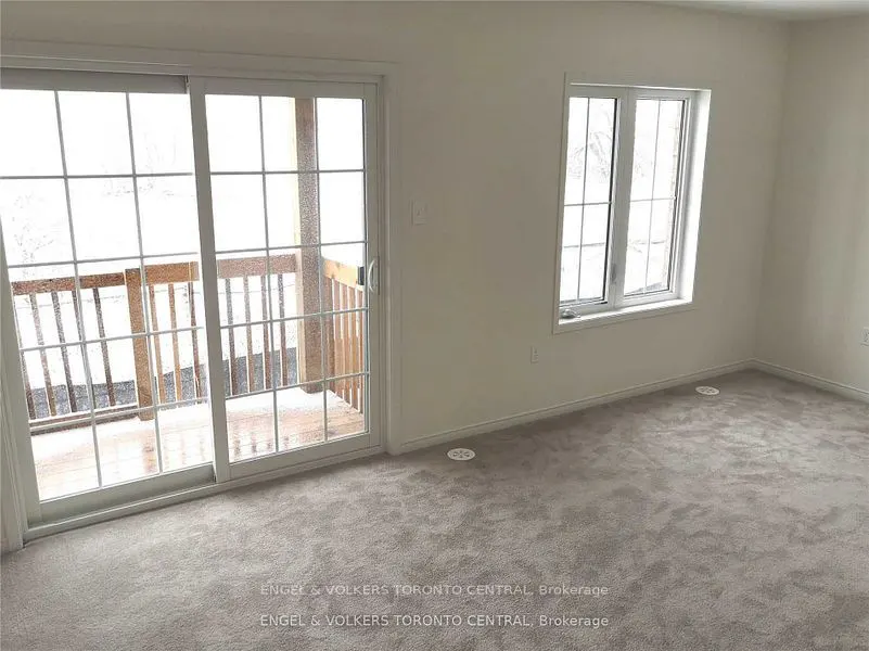 A bright, empty room with gray carpet, white walls, a window, and sliding glass doors to a snowy balcony.