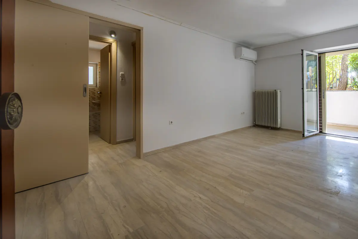 An empty room with marble floors, white walls, and an open door to a balcony with trees visible. A sliding door leads to a bathroom.
