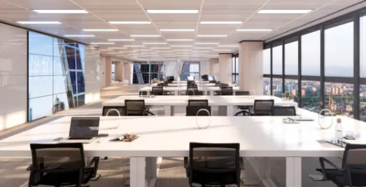 Bright, modern office space with white desks, black chairs, and large windows overlooking a city. A large screen displays the time.