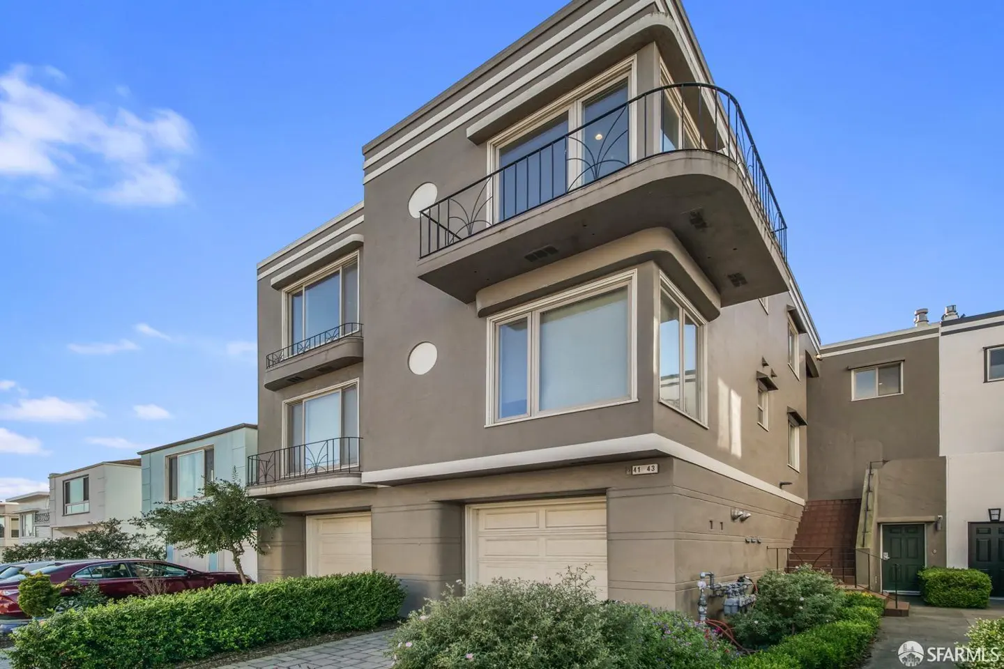 Exterior view of a modern, gray two-story home with a balcony, white trim, and two garage doors. Blue sky background.
