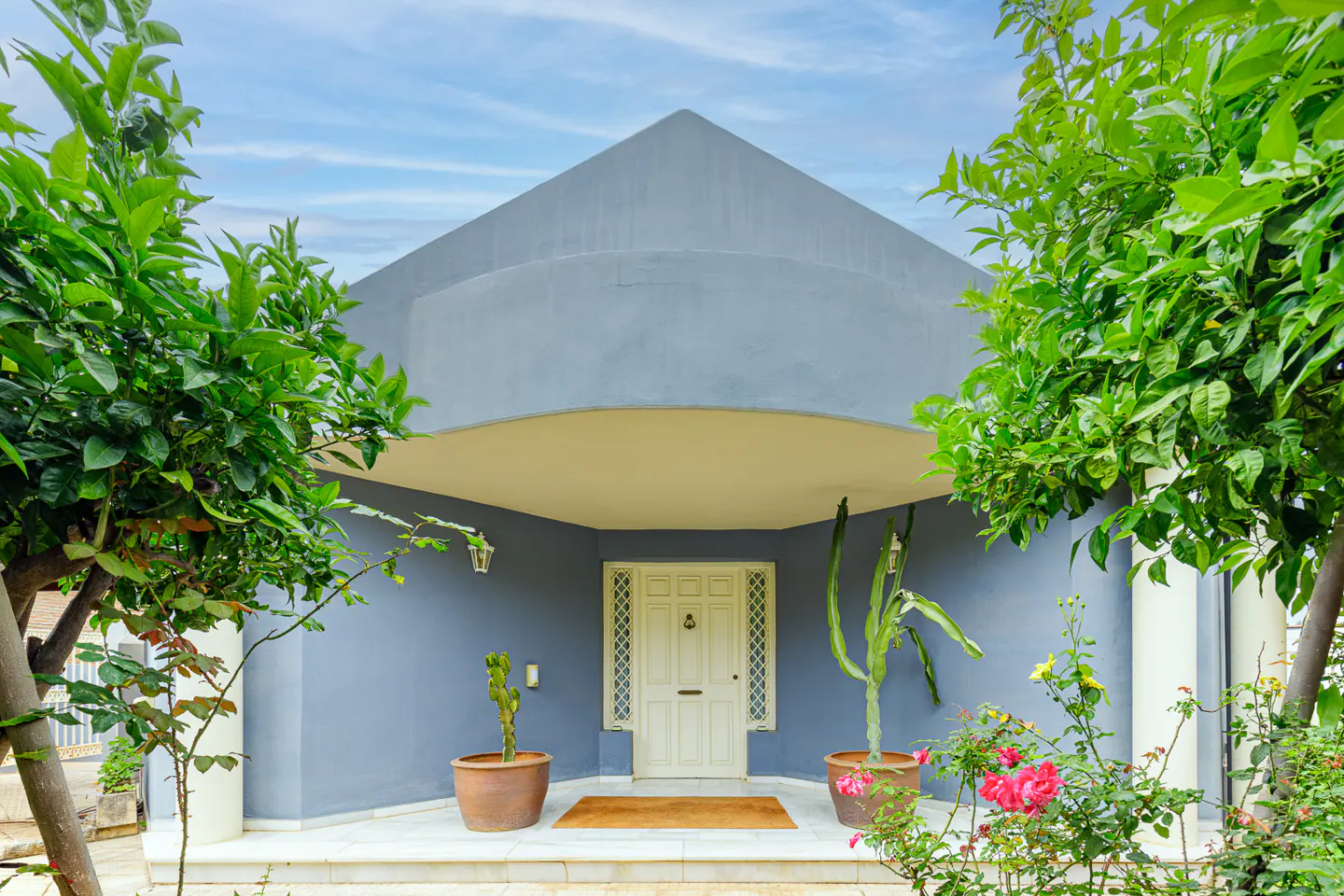 Front view of a blue house with a white door, plants, and a blue sky.