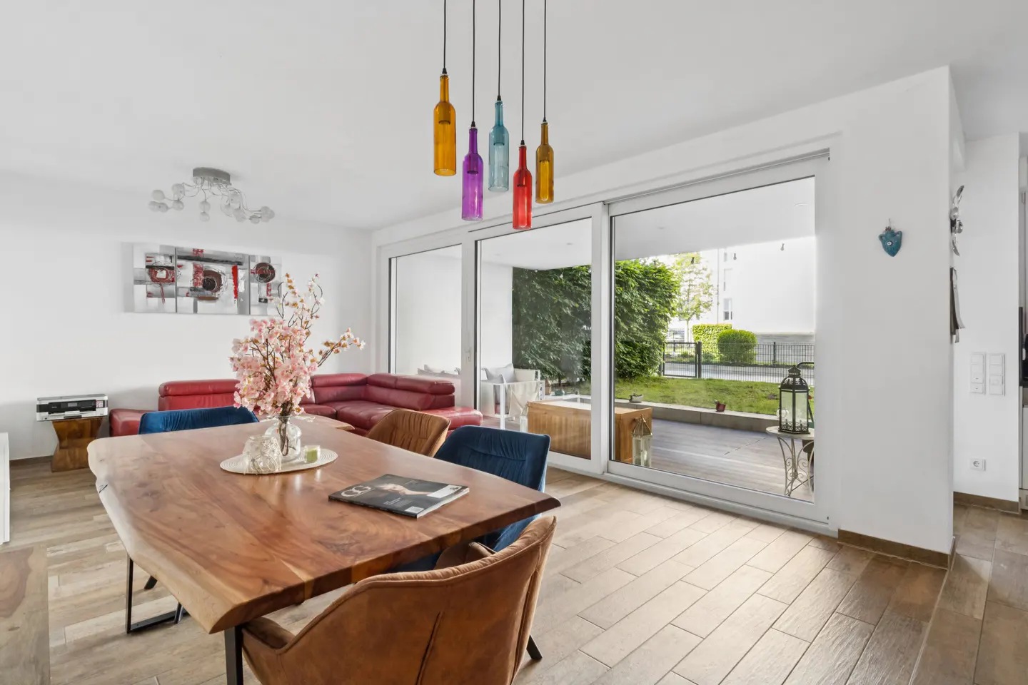 Bright living room with a wood table, colorful bottle lights, and a large sliding glass door to a patio.