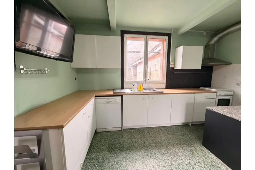 A kitchen with light green walls, white cabinets, wood countertops, and a TV mounted on the wall.
