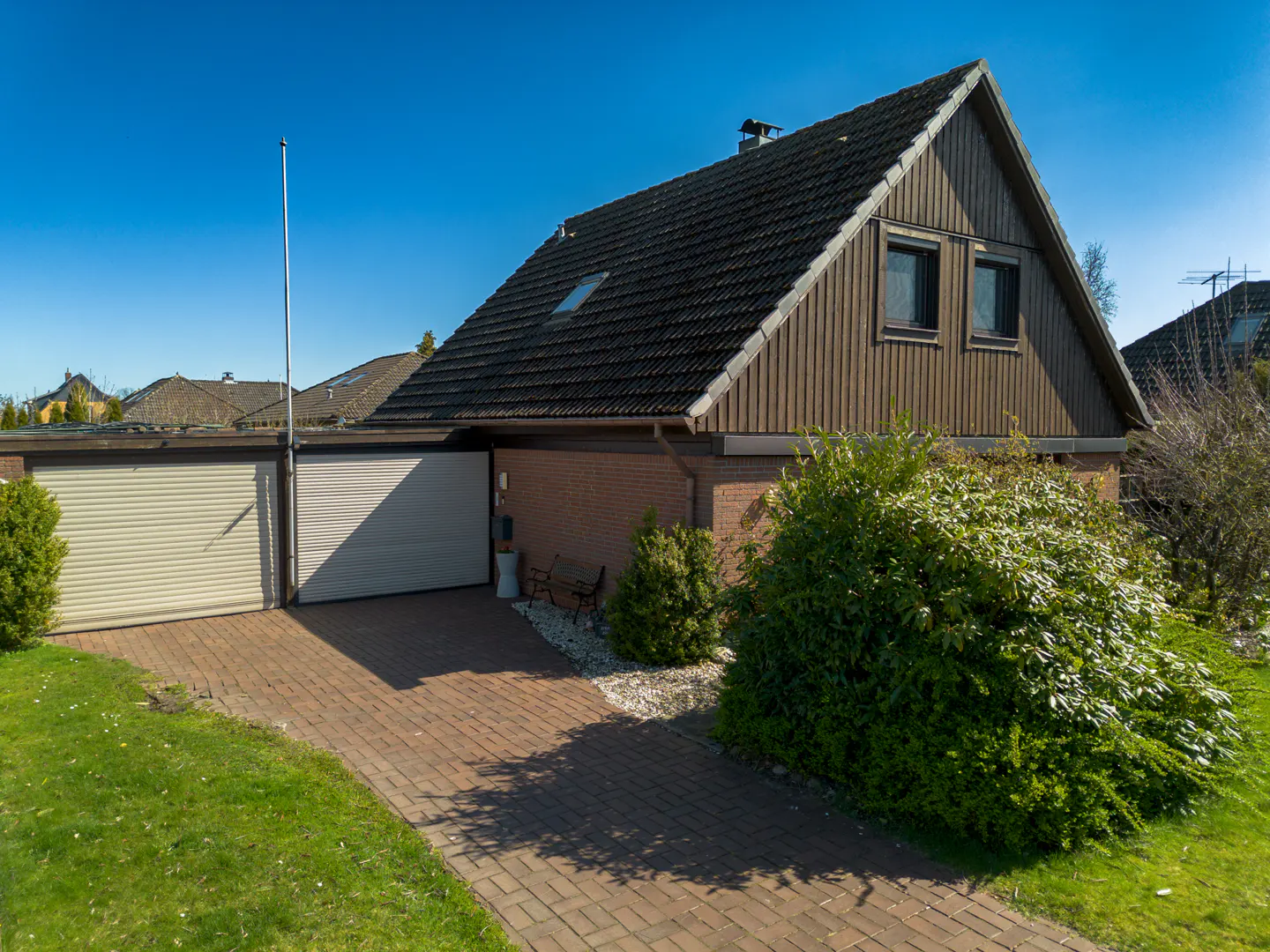 Exterior view of a single-family home with a brick driveway, two-car garage, and brown wood siding under a dark roof.