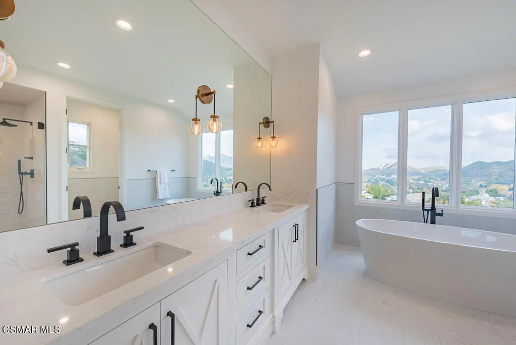 Bright bathroom with white cabinets, marble counters, and black fixtures. A large window overlooks a mountain view.