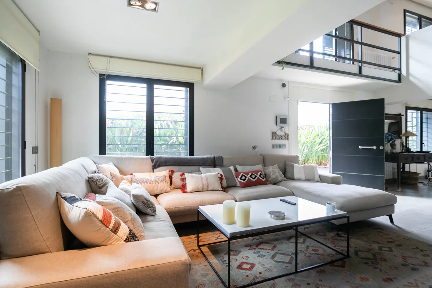 Modern living room with a large beige sectional sofa, patterned rug, white coffee table, and an open mezzanine level.