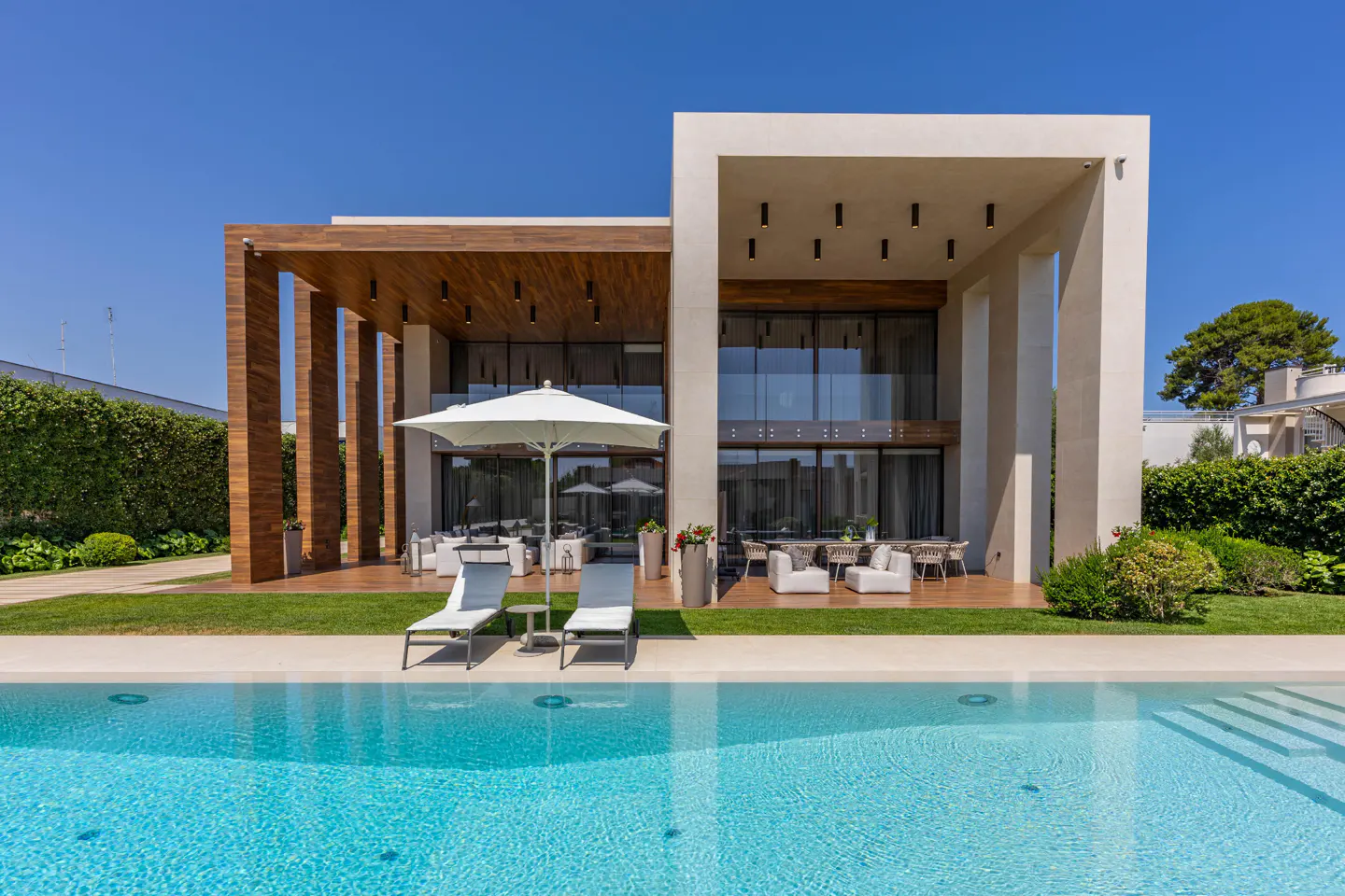 Modern two-story house with a pool. The house has wood and white accents, large windows, and outdoor seating.