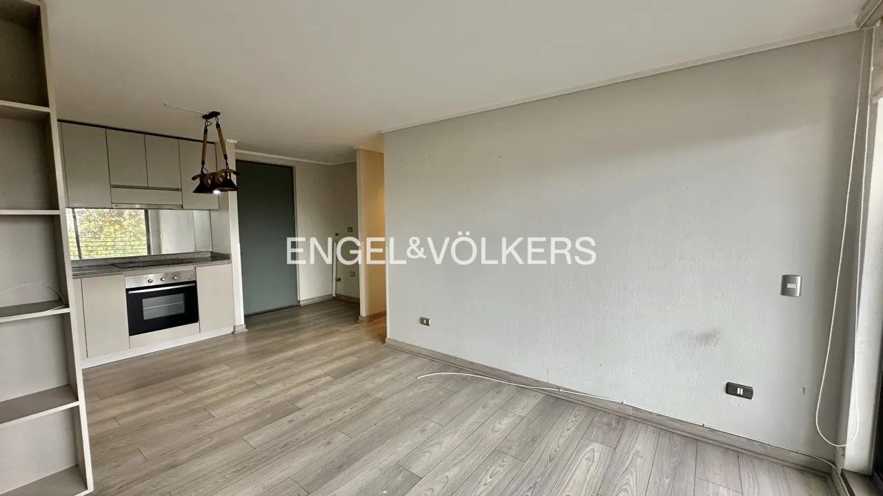 A bright, empty apartment with light wood floors, a kitchen with stainless steel appliances, and the Engel & Völkers logo.