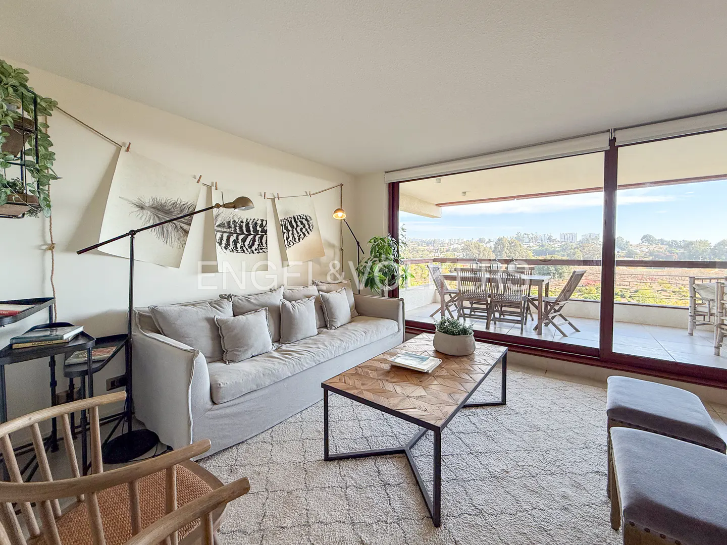 Living room with a gray sofa, patterned coffee table, and a balcony with outdoor furniture. Feather drawings hang on the wall.