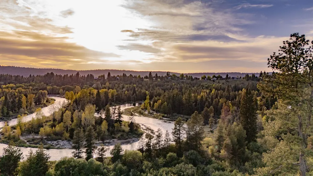 A winding river flows through a dense forest of evergreen and autumn trees under a golden sunset sky.