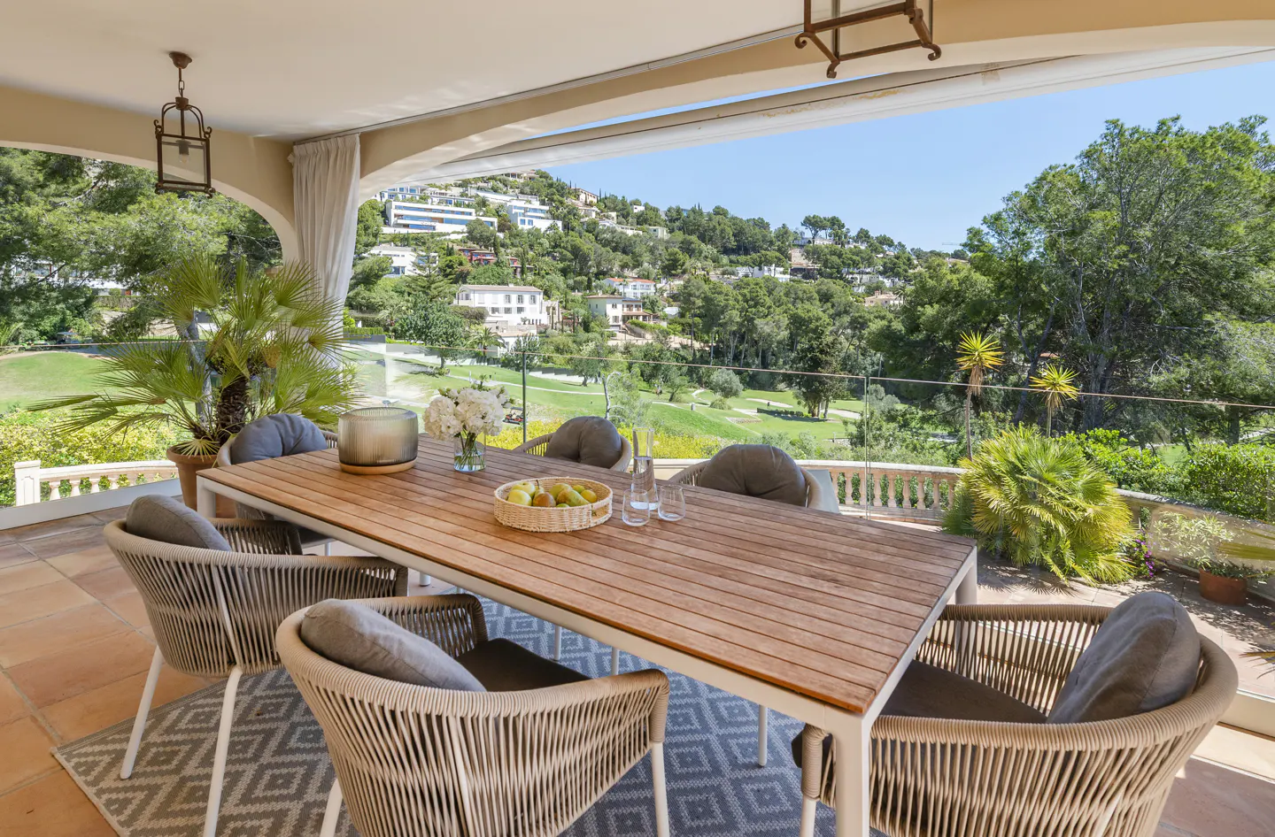 Outdoor dining area with a wooden table, wicker chairs, and a view of green hills and a golf course.