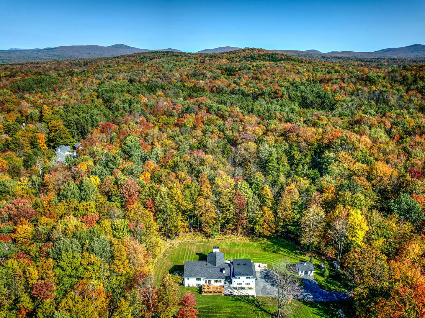 Aerial view of a house with a gray roof surrounded by colorful autumn trees and green grass.