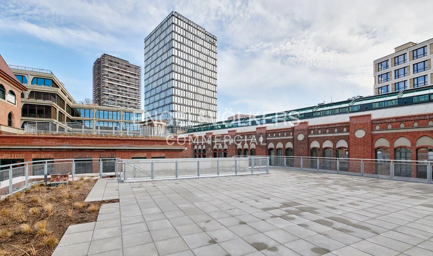 Rooftop view of brick buildings and modern glass skyscrapers under a cloudy sky. Gray tiled patio with metal railings.