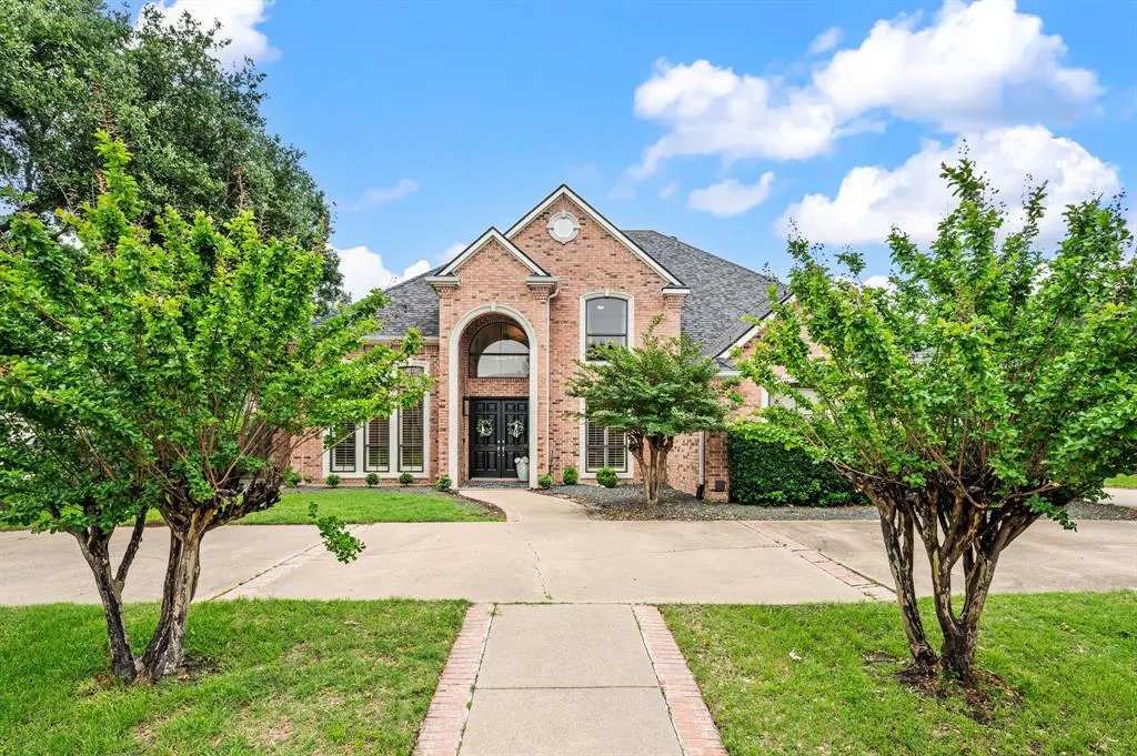 Two-story brick house with a gray roof, black double doors, and a large arched window above the entrance. Green trees frame the house.