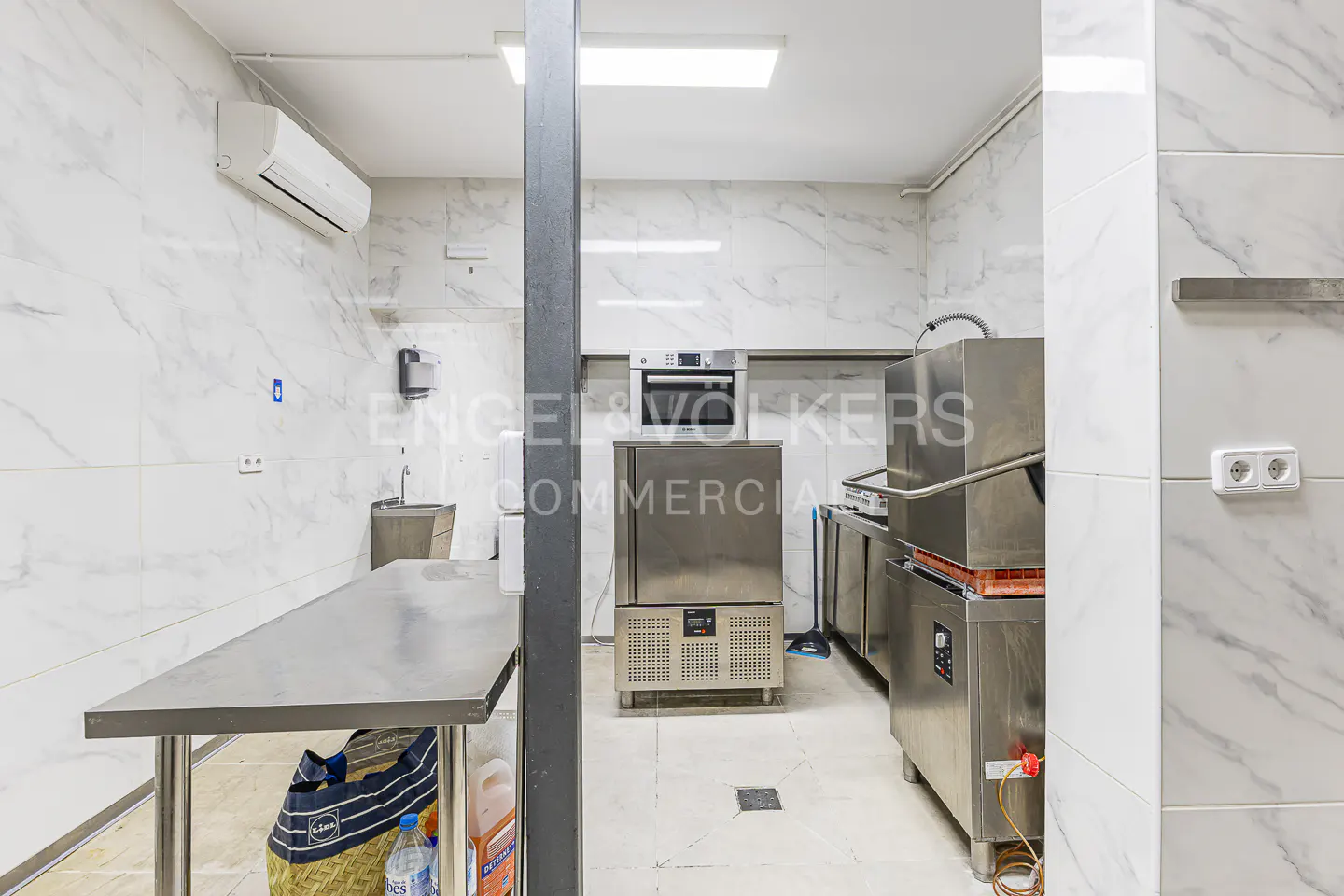 Commercial kitchen with stainless steel appliances, marble-patterned tiled walls, and a metal prep table.