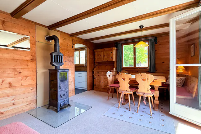A cozy dining room with wood-paneled walls, a black wood-burning stove, and a wooden table with chairs.