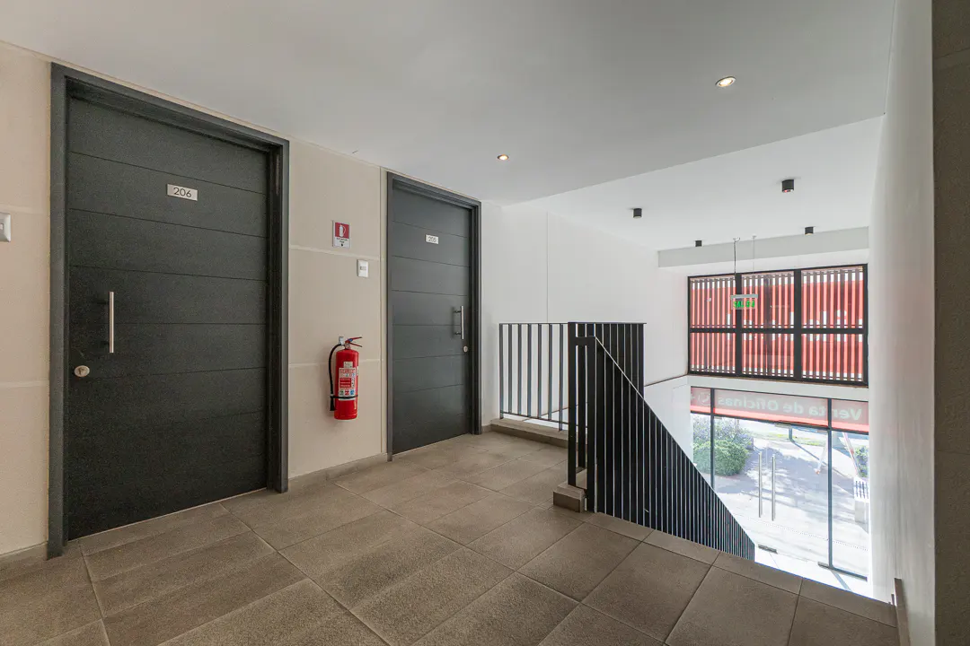 Hallway with two black doors, one labeled "206", a red fire extinguisher, and a staircase with black railings.