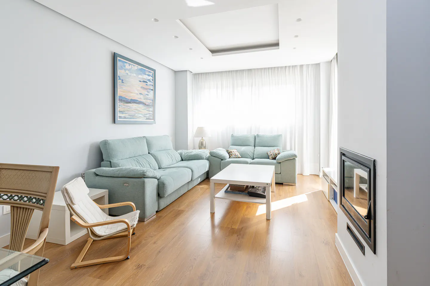 Bright living room with light blue sofas, white walls, and wood floors. A white coffee table sits in front of the sofas. A fireplace is on the right wall.
