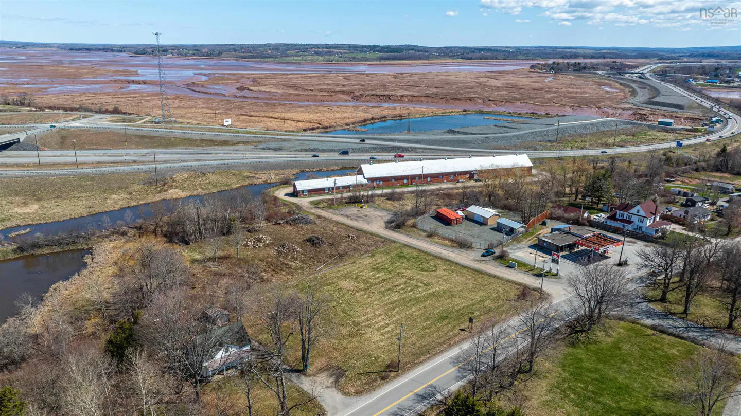 Aerial view of a rural landscape with a long red brick building, highway, and marshland under a blue sky.